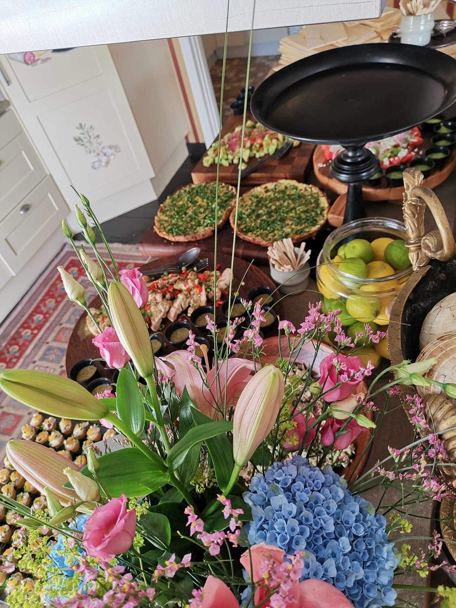 Blomsterarrangemang med rosa liljor och blå hortensia framför ett bord med tårtor.