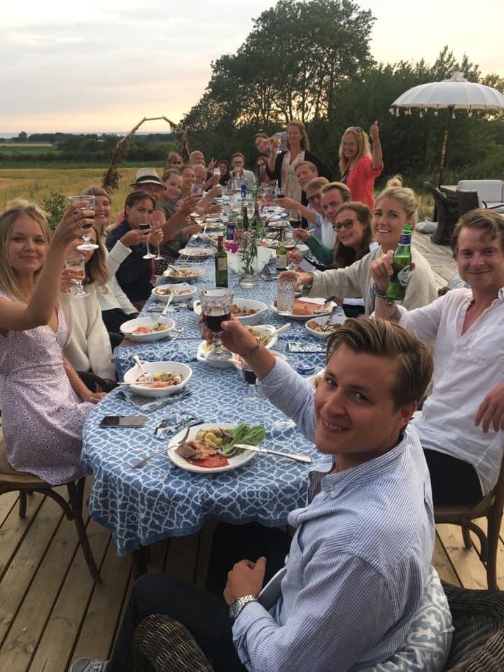 Ett långbord utomhus i solnedgången där gästerna höjer sina glas.