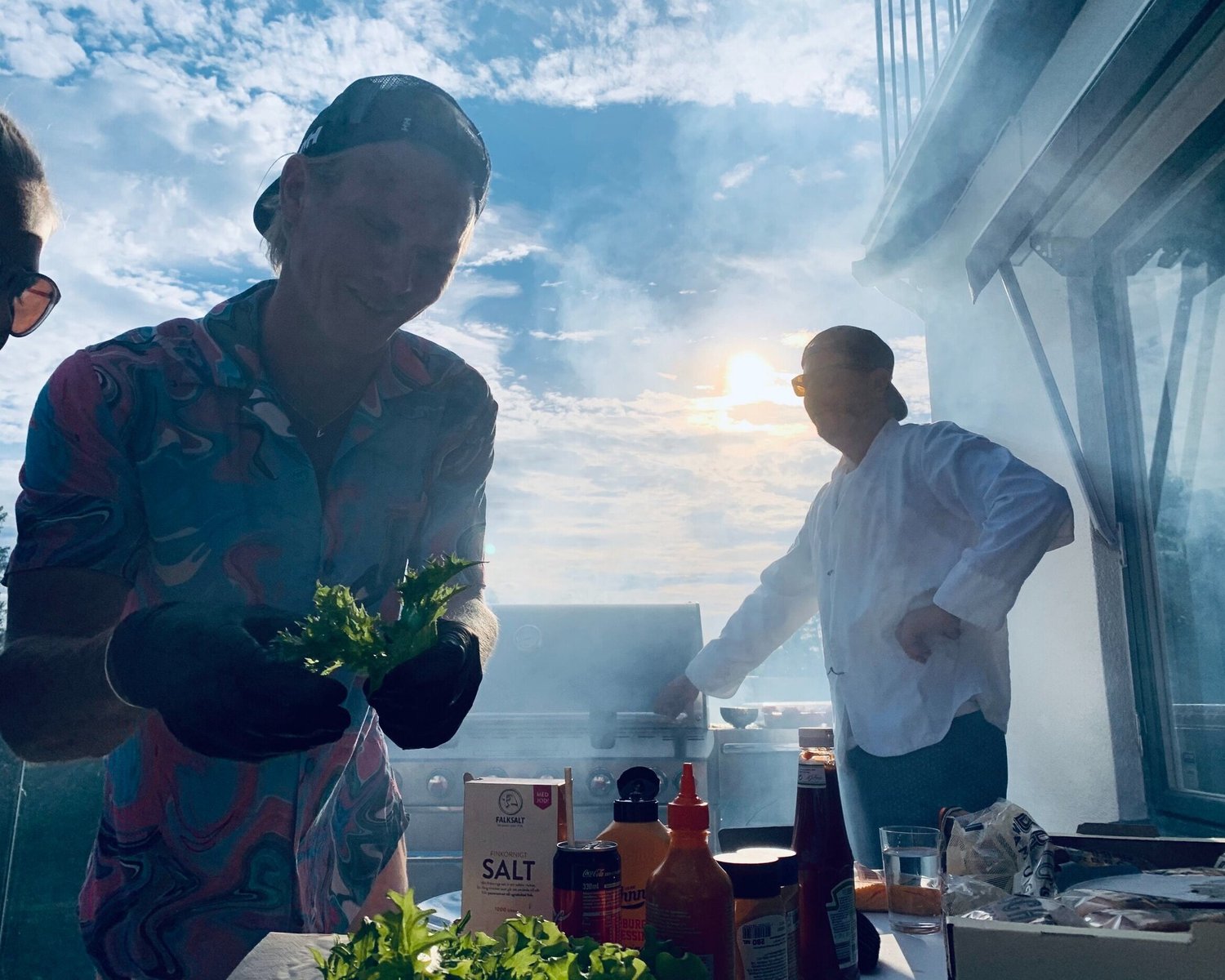 Matlagning vid grillen i kvällssol, där färsk sallad läggs upp.
